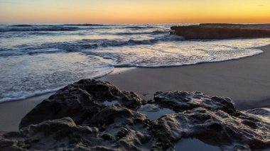 Günbatımında Güney Kaliforniya plaj manzarası. Antik resifler, gel-git havuzları, okyanus dalgaları, sörfçüler ve Swamis Resif Parkı Encinitas California 'da sıcak renkli gökyüzü..