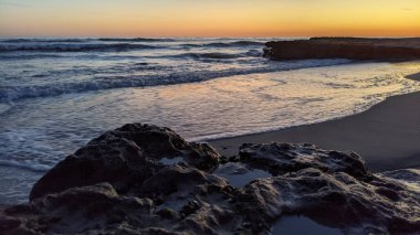 Günbatımında Güney Kaliforniya plaj manzarası. Antik resifler, gel-git havuzları, okyanus dalgaları, sörfçüler ve Swamis Resif Parkı Encinitas California 'da sıcak renkli gökyüzü..