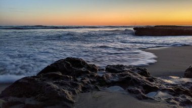 Günbatımında Güney Kaliforniya plaj manzarası. Antik resifler, gel-git havuzları, okyanus dalgaları, sörfçüler ve Swamis Resif Parkı Encinitas California 'da sıcak renkli gökyüzü..