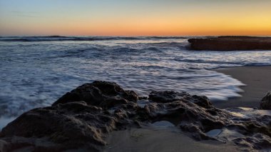Günbatımında Güney Kaliforniya plaj manzarası. Antik resifler, gel-git havuzları, okyanus dalgaları, sörfçüler ve Swamis Resif Parkı Encinitas California 'da sıcak renkli gökyüzü..