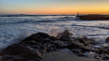 Günbatımında Güney Kaliforniya plaj manzarası. Antik resifler, gel-git havuzları, okyanus dalgaları, sörfçüler ve Swamis Resif Parkı Encinitas California 'da sıcak renkli gökyüzü..