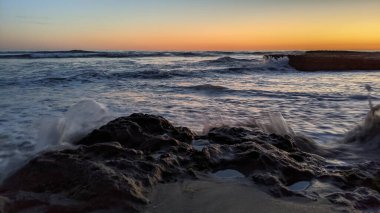 Günbatımında Güney Kaliforniya plaj manzarası. Antik resifler, gel-git havuzları, okyanus dalgaları, sörfçüler ve Swamis Resif Parkı Encinitas California 'da sıcak renkli gökyüzü..