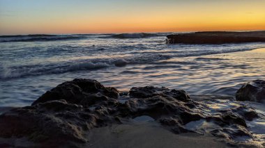 Günbatımında Güney Kaliforniya plaj manzarası. Antik resifler, gel-git havuzları, okyanus dalgaları, sörfçüler ve Swamis Resif Parkı Encinitas California 'da sıcak renkli gökyüzü..