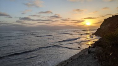 Günbatımında Güney Kaliforniya plaj manzarası. Antik resifler, gel-git havuzları, okyanus dalgaları, sörfçüler ve Swamis Resif Parkı Encinitas California 'da sıcak renkli gökyüzü..