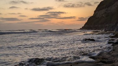 Swamis Resif Parkı Encinitas California 'da gelgit havuzları, soyut kaya oluşumları, okyanus dalgaları, sörfçüler ve sıcak renkli gökyüzü ile günbatımında Güney Kaliforniya plaj sahneleri.