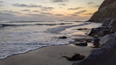 Swamis Resif Parkı Encinitas California 'da gelgit havuzları, soyut kaya oluşumları, okyanus dalgaları, sörfçüler ve sıcak renkli gökyüzü ile günbatımında Güney Kaliforniya plaj sahneleri.