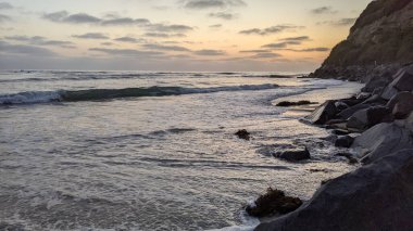 Swamis Resif Parkı Encinitas California 'da gelgit havuzları, soyut kaya oluşumları, okyanus dalgaları, sörfçüler ve sıcak renkli gökyüzü ile günbatımında Güney Kaliforniya plaj sahneleri.