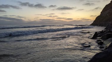 Güney Kaliforniya plaj sahneleri, gelgit havuzları, soyut kaya oluşumları, okyanus dalgaları, sörf tahtaları, palmiye ağaçları ve Swamis Resif Parkı Encinitas California 'da sıcak lavanta gökyüzü..