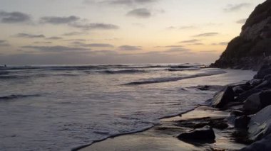 Günbatımında Güney Kaliforniya plaj sahneleri gelgit havuzları, siluetler, soyut kaya oluşumları, okyanus dalgaları, sörf tahtalı sörfçüler ve Swamis Resif Parkı Encinitas California 'da sıcak güneşli gökyüzü.