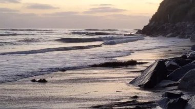 Günbatımında Güney Kaliforniya plaj sahneleri gelgit havuzları, siluetler, soyut kaya oluşumları, okyanus dalgaları, sörf tahtalı sörfçüler ve Swamis Resif Parkı Encinitas California 'da sıcak güneşli gökyüzü.