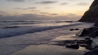 Günbatımında Güney Kaliforniya plaj sahneleri gelgit havuzları, siluetler, soyut kaya oluşumları, okyanus dalgaları, sörf tahtalı sörfçüler ve Swamis Resif Parkı Encinitas California 'da sıcak güneşli gökyüzü.
