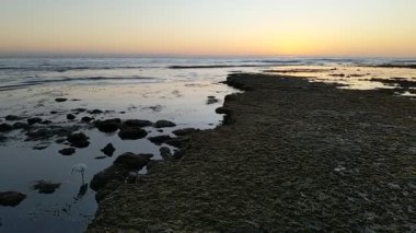 Günbatımında Güney Kaliforniya plaj sahneleri gelgit havuzları, siluetler, soyut kaya oluşumları, okyanus dalgaları, sörf tahtalı sörfçüler ve Swamis Resif Parkı Encinitas California 'da sıcak güneşli gökyüzü.