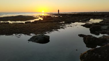 Günbatımında Güney Kaliforniya plaj sahneleri gelgit havuzları, siluetler, soyut kaya oluşumları, okyanus dalgaları, sörf tahtalı sörfçüler ve Swamis Resif Parkı Encinitas California 'da sıcak güneşli gökyüzü.