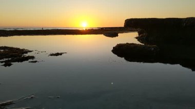 Günbatımında Güney Kaliforniya plaj sahneleri gelgit havuzları, siluetler, soyut kaya oluşumları, okyanus dalgaları, sörf tahtalı sörfçüler ve Swamis Resif Parkı Encinitas California 'da sıcak güneşli gökyüzü.