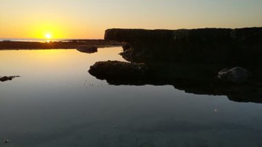 Günbatımında Güney Kaliforniya plaj sahneleri gelgit havuzları, siluetler, soyut kaya oluşumları, okyanus dalgaları, sörf tahtalı sörfçüler ve Swamis Resif Parkı Encinitas California 'da sıcak güneşli gökyüzü.
