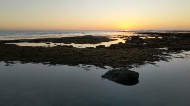 Günbatımında Güney Kaliforniya plaj sahneleri gelgit havuzları, siluetler, soyut kaya oluşumları, okyanus dalgaları, sörf tahtalı sörfçüler ve Swamis Resif Parkı Encinitas California 'da sıcak güneşli gökyüzü.