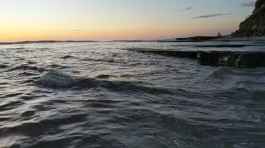 Güney Kaliforniya plaj sahnesi 4K video gelgit havuzları, soyut kaya oluşumları, okyanus dalgaları, sörf tahtaları ile sörfçüler Swamis Resif Parkı Encinitas California 'da sıcak güneşli gökyüzü.