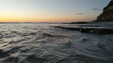 Güney Kaliforniya plaj sahnesi 4K video gelgit havuzları, soyut kaya oluşumları, okyanus dalgaları, sörf tahtaları ile sörfçüler Swamis Resif Parkı Encinitas California 'da sıcak güneşli gökyüzü.