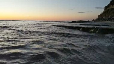 Güney Kaliforniya plaj sahnesi 4K video gelgit havuzları, soyut kaya oluşumları, okyanus dalgaları, sörf tahtaları ile sörfçüler Swamis Resif Parkı Encinitas California 'da sıcak güneşli gökyüzü.