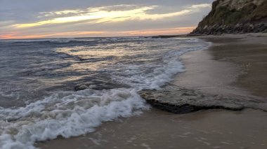 San Diego 'nun kuzeyinde Güney Kaliforniya sahilleri - Encinitas Kaliforniya' daki Swamis Resif Sörf Parkı 'nda günbatımı, sörfçüler, gelgit havuzları, dalgalar, kayalar, kum ve palmiye ağaçları.