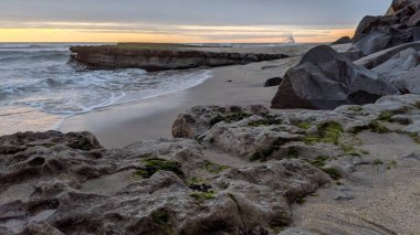 San Diego 'nun kuzeyinde Güney Kaliforniya sahilleri - Encinitas Kaliforniya' daki Swamis Resif Sörf Parkı 'nda günbatımı, sörfçüler, gelgit havuzları, dalgalar, kayalar, kum ve palmiye ağaçları.