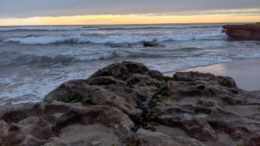 San Diego 'nun kuzeyinde Güney Kaliforniya sahilleri - Encinitas Kaliforniya' daki Swamis Resif Sörf Parkı 'nda günbatımı, sörfçüler, gelgit havuzları, dalgalar, kayalar, kum ve palmiye ağaçları.