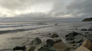 Güney Kaliforniya sahilleri San Diego 'nun kuzeyinde. Sahil şeridi günbatımları, okyanus dalgaları, sörfçüler, gelgit havuzları, palmiye ağaçları ve Encinitas California 'daki Swamis Resif Sörf Parkı' ndaki kaya soyutlamaları..