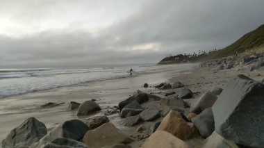 Güney Kaliforniya sahilleri San Diego 'nun kuzeyinde. Sahil şeridi günbatımları, okyanus dalgaları, sörfçüler, gelgit havuzları, palmiye ağaçları ve Encinitas California 'daki Swamis Resif Sörf Parkı' ndaki kaya soyutlamaları..