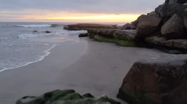 Swamis Sahili üzerinde günbatımı gökyüzü. Güney Kaliforniya 'da uzak kumsallar, günbatımları, sörfçüler, gelgit havuzları, dalgalar yontulmuş kayalar, palmiye ağaçları ve San Diego' nun kuzeyindeki Encinitas sahillerindeki Swamis Resif Sörf Parkı 'nda şiddetli kış fırtınaları..