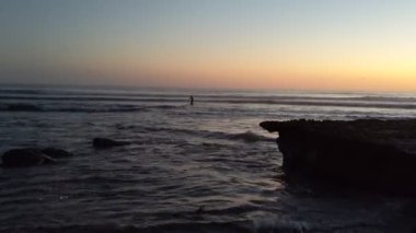 Swamis Sahili üzerinde günbatımı gökyüzü. Güney Kaliforniya 'da uzak kumsallar, günbatımları, sörfçüler, gelgit havuzları, dalgalar yontulmuş kayalar, palmiye ağaçları ve San Diego' nun kuzeyindeki Encinitas sahillerindeki Swamis Resif Sörf Parkı 'nda şiddetli kış fırtınaları..