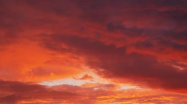 Koyu kırmızı ve turuncu bulutlardan oluşan ateşli bir tablo gökyüzünü dolduruyor ve yoğun ve dramatik bir atmosfer yaratıyor.