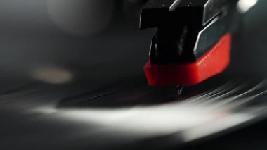 Dönen vinil plakta kırmızı ve siyah bir iğnenin yakın çekimi, oyukları ve yansımaları yakalıyor..