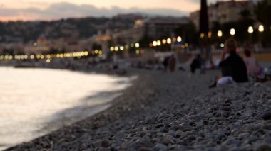 Gün batımından sonra sahilde dinlenip denize çakıl taşları atan tanınmamış insanlar. Güzelmiş. Sığ alan derinliği.