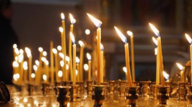 Altın tutacaklara yerleştirilmiş sayısız mum. Alevler parlak ve sabit. Arka plan karanlık ama mum ışığıyla aydınlatılmış..