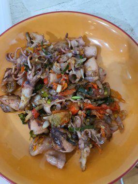 Endonezya 'nın geleneksel sokak yemekleri olan tumis cumi hitam sotelenmiş küçük siyah mürekkep balıkları gri arka planda servis edilir.