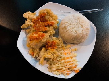 Ateşli Tavuk Geprek Cazibesi: Beyaz Tabakta Baharatlı Tavuk Geprek, Pirinç ve Sebzelerin Yakın Çekimi