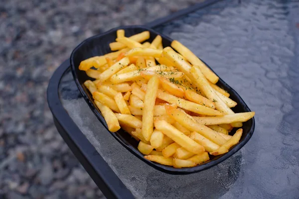 Lezzetli patates kızartması, cam bir masada siyah bir tabakta sunuluyor.