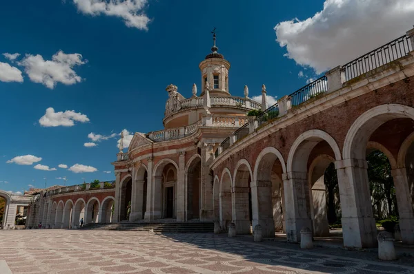 İspanya. Aranjuez. Kraliyet Sarayı 'nın çarşısı. Pencereli çatısı var. Yeşil çimenler. Royal Palace 'ın yanına park et. Taho Nehri. Sarayın yakınındaki kanal. Kanalın üzerindeki köprü. Mavi gökyüzü, beyaz bulutlar.