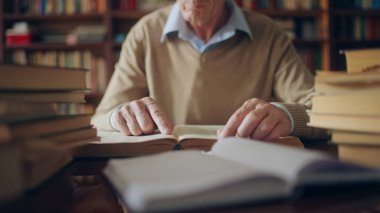 Senior researcher studying literature sitting in the library, stacks of books around