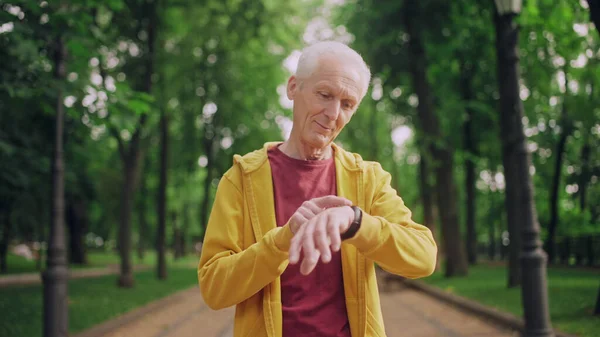 Senior man checking activity indicators on wrist fitness tracker after workout