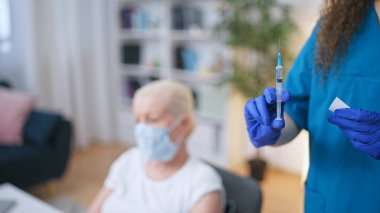 Koruyucu eldiven takan tıp çalışanı, elinde sıvı dolu bir şırınga tutuyor, iğneyi yapmaya hazır.