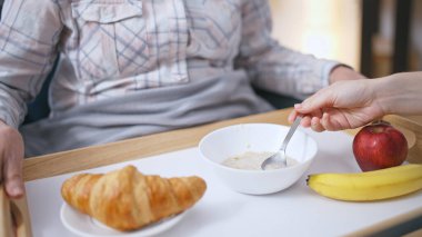 Bakıcı kız annesini kaşıkla besliyor, olgun kadının iyileşmesine yardım ediyor.