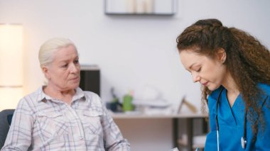 Yaşlı bir kadına ilaç yazan genç bir doktor, ev ziyareti.