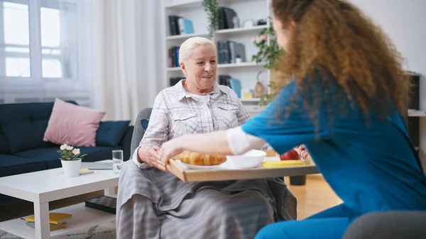Retirement home nurse bringing meal to a senior woman, taking care of a tenant