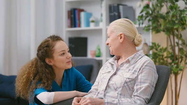 Bakıcı hemşire huzurevinde örgü ören yaşlı kadını ziyaret ediyor.