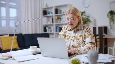 Ciddi, olgun bir kadın dizüstü bilgisayarına odaklanmış, uzaktan mali analist.