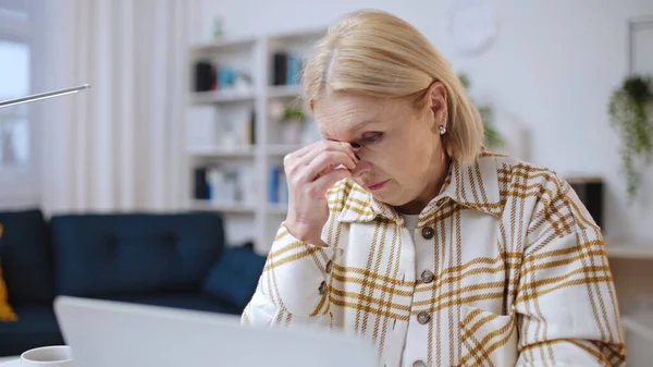 Tired senior woman got an email with bad news while working on laptop, failure, trouble