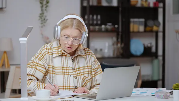 一位50多岁的妇女正在上在线课程 观看视频课程 记录笔记 — 图库照片