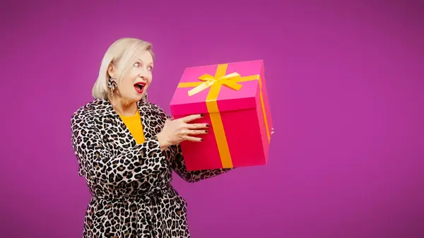 A senior woman is holding a large gift box and wondering what\'s inside, a birthday present