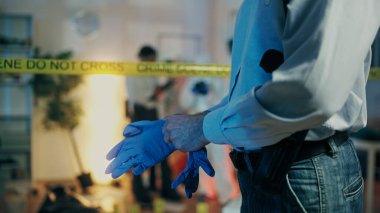 Bir dedektif, cinayet soruşturması sırasında darmadağın olmuş dairedeki suç mahallini incelemek için eldiven takıyor.